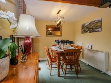 A dining room with a wooden table and chairs set with plates and glasses at Columbine Cottage in Hawkshead