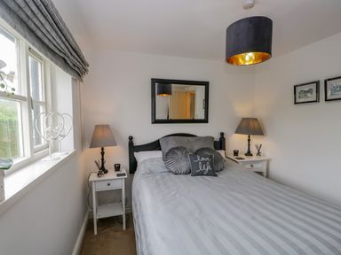 A bedroom with a bed gray bedding two bedside tables with lamps window with gray curtains and a mirror on the wall at Columbine Cottage in Hawkshead