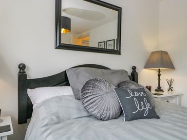 A bedroom with a black headboard bed gray pillows a lamp and a mirror at Columbine Cottage in Hawkshead