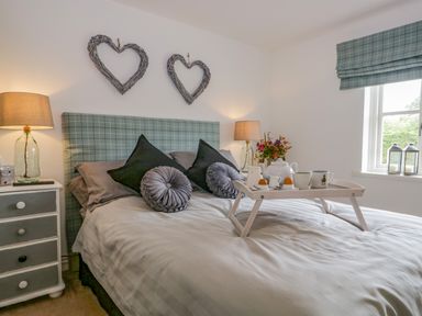 A bedroom with a bed with pillows and a breakfast tray a nightstand with a lamp on each side and two heart-shaped wall decorations at Columbine Cottage in Hawkshead