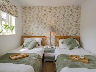 A bedroom with two single beds a nightstand with a lamp and floral wallpaper at Columbine Cottage in Hawkshead