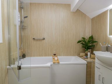 A bathroom with a bathtub shower combination a plant and toiletries at Columbine Cottage in Hawkshead