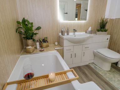 A bathroom with a bathtub holding a candle and a glass of wine a sink with toiletries and a toilet at Columbine Cottage in Hawkshead