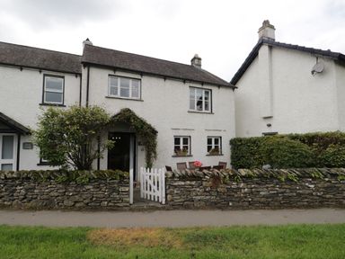 A stone wall with a white gate in front of a two-story building with a patio table and chairs at Columbine Cottage in Hawkshead