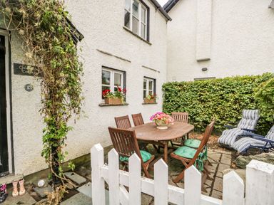 An outdoor patio area with a wooden table and chairs with cushions and a potted plant on the table at Columbine Cottage in Hawkshead