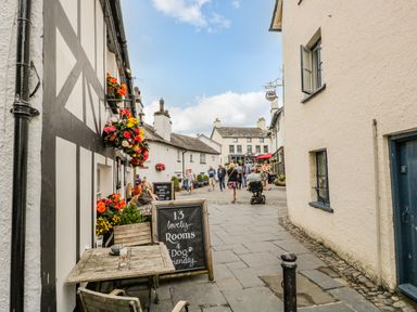 A street with people walking and a building with flowers and a chalkboard sign at Columbine Cottage in Hawkshead