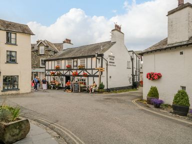 A street view with a traditional pub building with flowers on windows and people sitting outside at Columbine Cottage in Hawkshead