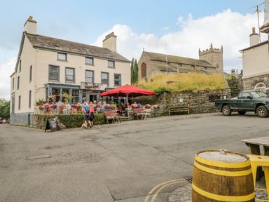 An outdoor seating area with tables and a red umbrella next to a cream building with a sign reading Poppied at Columbine Cottage in Hawkshead