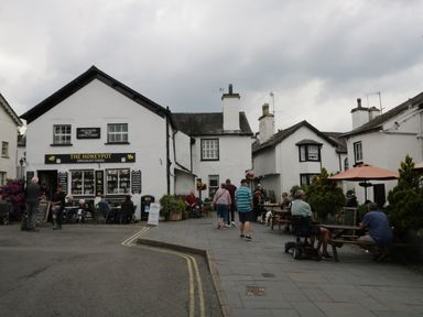 An outdoor seating area with people sitting and walking near white buildings including The Honeypot specialist foods at Columbine Cottage in Hawkshead