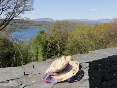 Stone wall with two straw hats and sunglasses overlooking trees lake and distant mountains at Columbine Cottage in Hawkshead