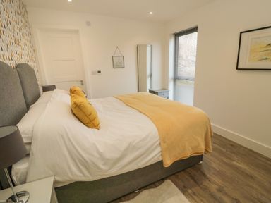 A bedroom with a double bed with yellow pillows and blanket a bedside lamp a full-length mirror and framed pictures at Forget Me Not Lodge Bamburgh