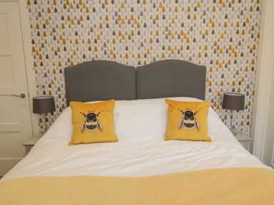 A bedroom with a double bed two yellow bee cushions gray headboard nightstands and lamps at Forget Me Not Lodge in Bamburgh