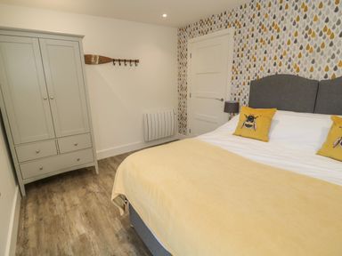 A bedroom with a double bed with yellow bee pillows and a yellow blanket a grey wardrobe and a wooden oar with hooks on the wall at Forget Me Not Lodge Bamburgh