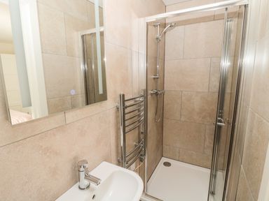 A bathroom with a sink a mirror a towel radiator and a glass shower enclosure at Forget Me Not Lodge Bamburgh