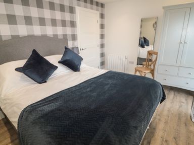 A bedroom with a bed, two pillows, a wooden chair, a full-length mirror, and a wardrobe at Forget Me Not Lodge in Bamburgh