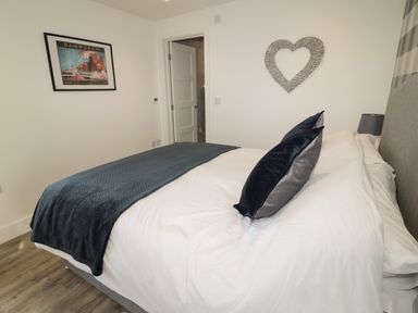 A bedroom with a bed white bedding blue throw pillows and blanket a framed picture and heart wall decor at Forget Me Not Lodge in Bamburgh