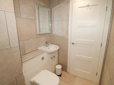 A small bathroom with a toilet sink unit mirror and a closed white door at Forget Me Not Lodge in Bamburgh