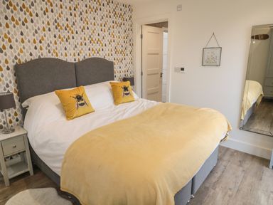 A bedroom with a bed with yellow pillows and throw next to a bedside table with a lamp and a wall mirror at Forget Me Not Lodge in Bamburgh