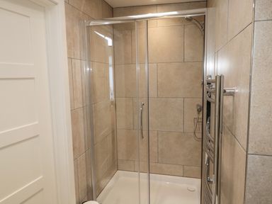 A shower enclosure with sliding glass doors and beige tiled walls at Forget Me Not Lodge in Bamburgh