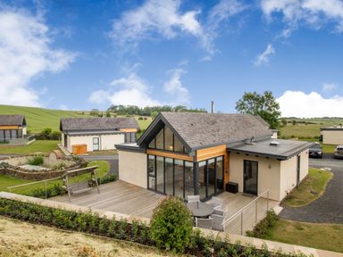 A modern house with a wooden deck patio and outdoor seating in a rural area at Forget Me Not Lodge in Bamburgh
