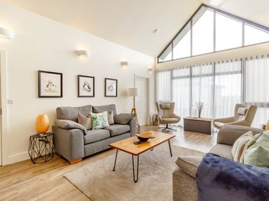 A living room with two gray sofas a wooden coffee table two beige armchairs and three framed pictures on the wall at Forget Me Not Lodge in Bamburgh