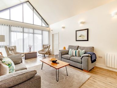 A living room with two grey sofas two beige chairs a wooden coffee table and large windows at Forget Me Not Lodge Bamburgh