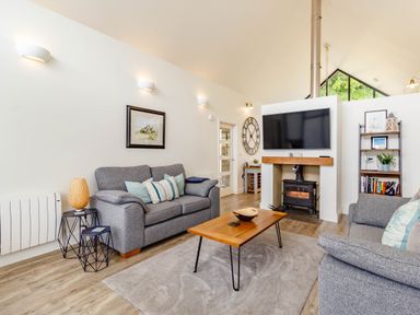 A living room with two gray sofas a wooden coffee table a fireplace with a mounted TV and a bookshelf at Forget Me Not Lodge in Bamburgh