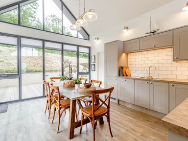 A kitchen with gray cabinets wooden dining table six chairs and large windows at Forget Me Not Lodge in Bamburgh