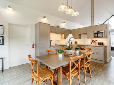 A kitchen with wooden chairs around a table and grey cabinets at Forget Me Not Lodge in Bamburgh