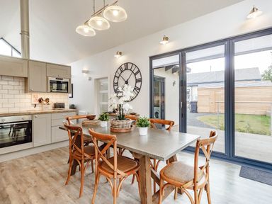 A dining area with wooden chairs and a table next to a kitchen with cabinets and oven at Forget Me Not Lodge Bamburgh