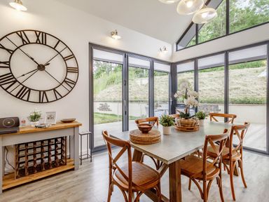 A dining area with a table and six chairs next to large glass windows and a wood wine rack at Forget Me Not Lodge in Bamburgh