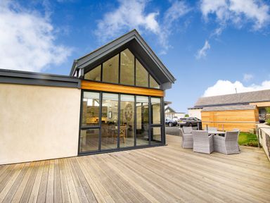 A house with large glass windows and a wooden deck with outdoor furniture at Forget Me Not Lodge in Bamburgh