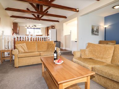 A living room with two sofas a wooden coffee table with wine and fruit and visible kitchen area at Tilly Mint Cottage Nr Ullswater