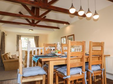 A dining area with wooden table and chairs with blue cushions and a living room with sofas in the background at Tilly Mint Cottage Nr Ullswater