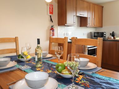 A dining table set with bowls plates wine glasses a bottle of wine and fruit in a kitchen at Tilly Mint Cottage Nr Ullswater