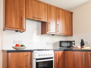A kitchen with wooden cabinets a white stove a microwave and a countertop with vegetables bread and knives at Tilly Mint Cottage Nr Ullswater