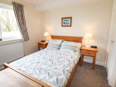A bedroom with a wooden double bed with floral bedding two bedside tables with lamps and a window with curtains at Tilly Mint Cottage Nr Ullswater