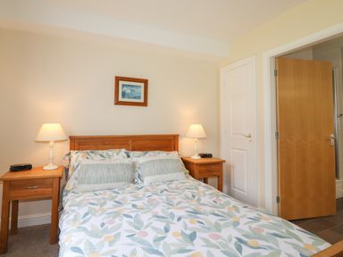 A bedroom with a bed with floral bedding two bedside tables with lamps and an open door at Tilly Mint Cottage Nr Ullswater