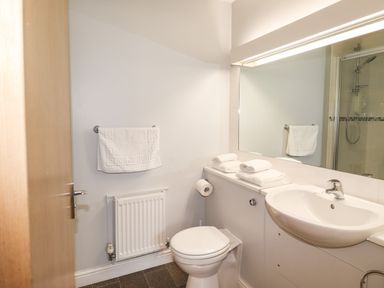A bathroom with a toilet a sink a mirror a towel rack with a towel and folded towels on the toilet at Tilly Mint Cottage Nr Ullswater