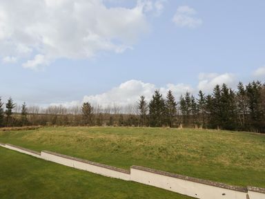 A grassy hill with a white low wall and trees in the background at Tilly Mint Cottage Nr Ullswater