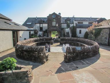 An outdoor courtyard with a large circular stone chessboard and houses in the background at Tilly Mint Cottage Nr Ullswater