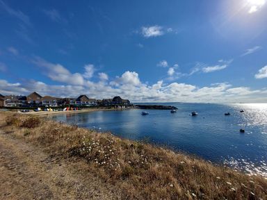 A coastal scene with houses along the shore boats on the water and grassy land in the foreground at Chesil Retreat in Weymouth