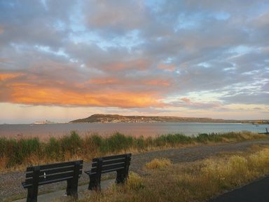A coastal view with two benches overlooking water and a distant town under a cloudy sky at Chesil Retreat in Weymouth