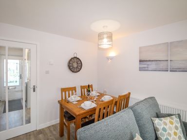 A dining area with a wooden table set for four near a gray sofa and glass-paneled door at Chesil Retreat in Weymouth