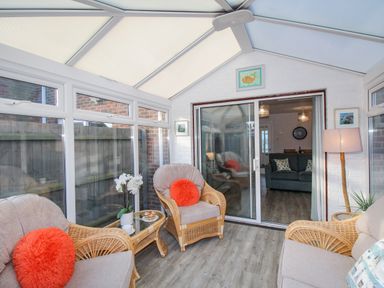 A conservatory with wicker chairs and orange cushions and a glass table at Chesil Retreat Weymouth