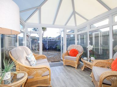A conservatory with wicker furniture and a glass table leading to a garden at Chesil Retreat in Weymouth