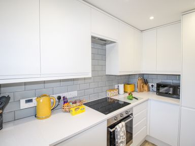 A kitchen with white cupboards a yellow kettle and toaster a microwave oven and cooking utensils at Chesil Retreat in Weymouth