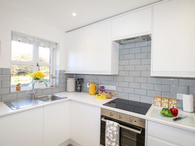 A kitchen with white cabinets a stainless steel sink a stove and yellow and green vegetables on the counter at Chesil Retreat in Weymouth
