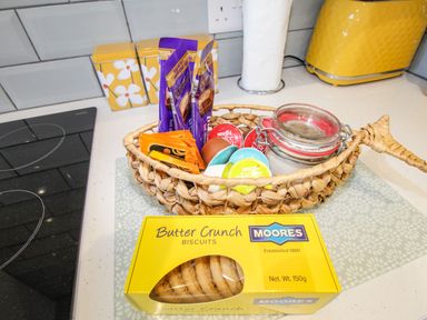 A kitchen counter with a basket of coffee pods and sachets next to a box of butter crunch biscuits and a yellow toaster at Chesil Retreat in Weymouth