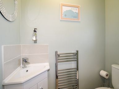 A bathroom with a corner sink mirror towel radiator toilet paper holder and framed map at Chesil Retreat in Weymouth